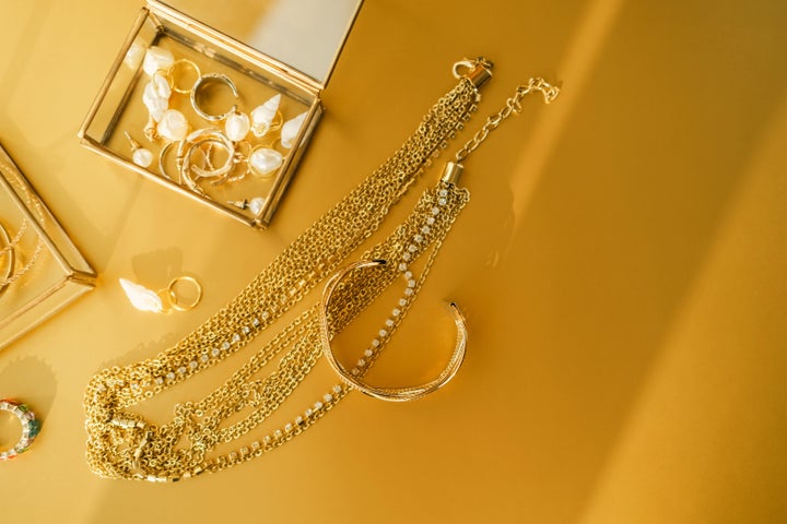 Top view of illuminated gold and pearl jewelry in glass boxes and on yellow metal surface.