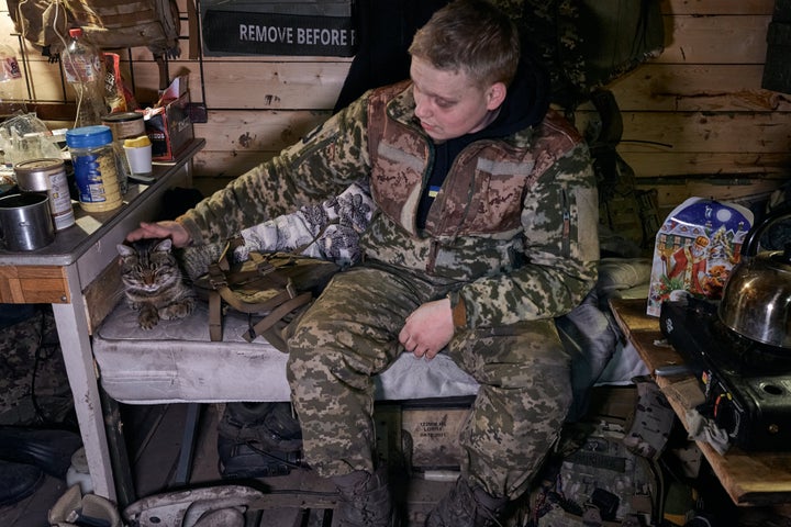 A Ukrainian soldier pets his cat Wednesday during a visit by a public relations officer with the 10th Edelweiss Brigade who wore a St. Nicholas costume as he presented candy packs to soldiers on the front line in Ukraine's Bukhmut District.