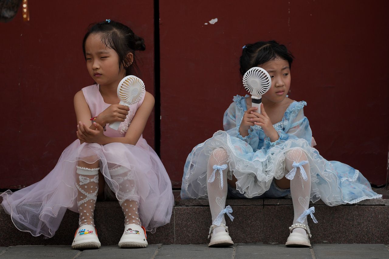Πιτσιρίκια στο Πεκίνο της Κίνας δροσίζονται με ανεμιστηράκια από τον ανυπόφορο καύσωνα με τις θερμοκρασίες-ρεκόρ του Ιουνίου. 