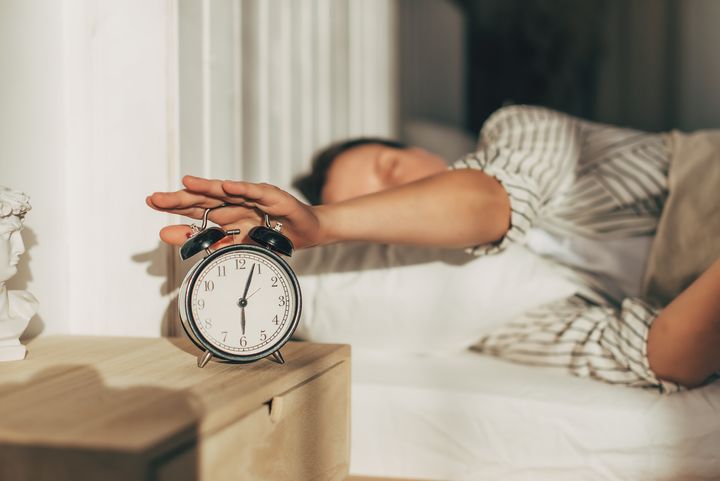Young sleeping woman and alarm clock in bedroom at home