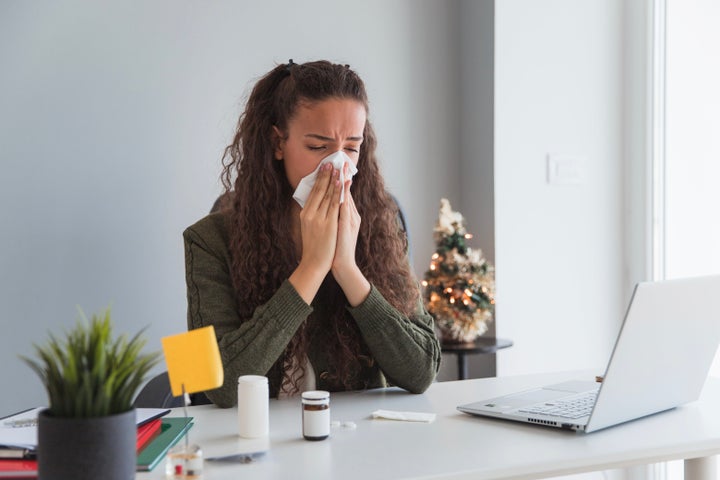 Sick young woman blowing her nose at work