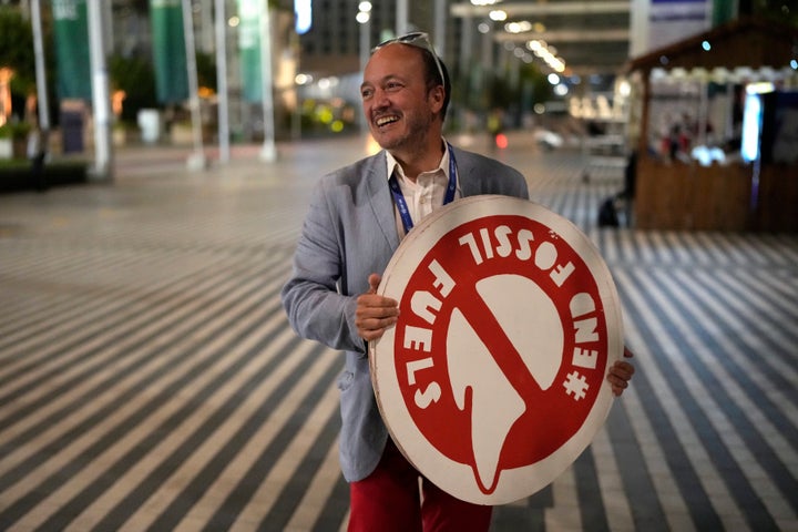 A man holds a sign that reads end fossil fuels at the COP28 U.N. Climate Summit as negotiations continue, Tuesday, Dec. 12, 2023, in Dubai, United Arab Emirates.