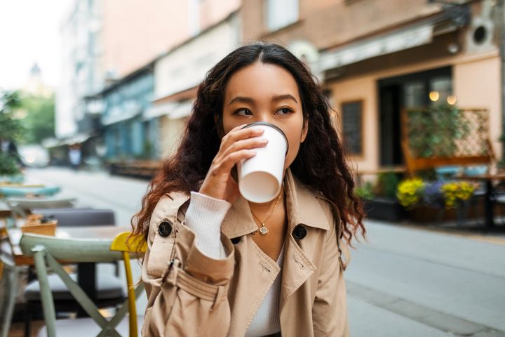 Young Asian woman drinking coffee in sidewalk cafe