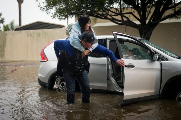 Santa Barbara Police Dept. detective Bryce Ford helps a motorist out of her car on a flooded street during a rainstorm, on Dec. 21, 2023, in Santa Barbara, Calif.