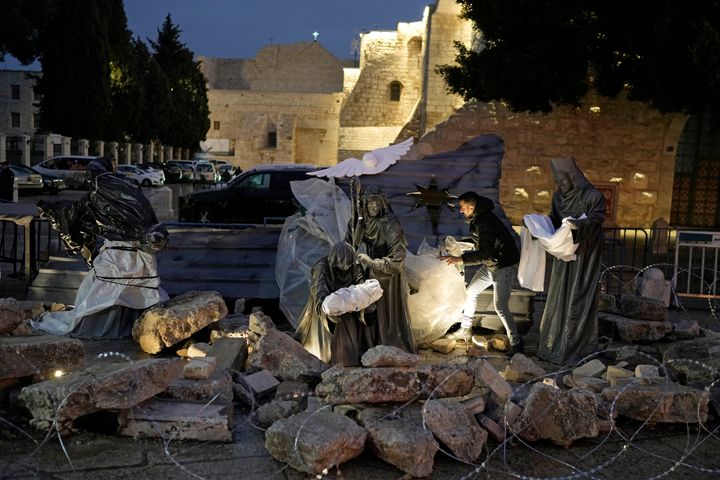 A man decorates a nativity scene with rubble around symbolizing the destruction in Gaza and white sheets referring to the dead civilians, in Manger Square, adjacent to the Church of the Nativity, in Bethlehem, Friday, Dec. 23, 2023. Bethlehem is having a subdued Christmas after officials in Jesus' traditional birthplace decided to forgo celebrations due to the Israel-Hamas war.(AP Photo/Leo Correa)