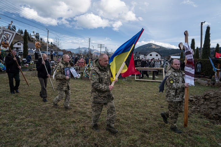 Ukrainian servicemen carry national flags and photos of their comrade Vasyl Boichuk who was killed in Mykolayiv in March 2022, during his funeral ceremony at the cemetery in Iltsi village, Ukraine, on Dec. 26, 2023.