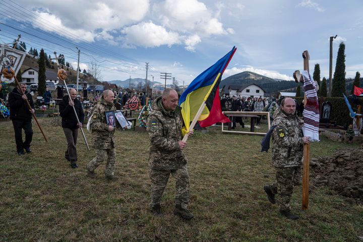 Ukrainian servicemen carry national flags and photos of their comrade Vasyl Boichuk who was killed in Mykolayiv in March 2022, during his funeral ceremony at the cemetery in Iltsi village, Ukraine, on Dec. 26, 2023. 