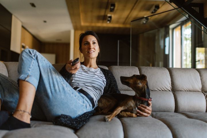 Woman in her early 40s relaxing with her pet dog at home, watching TV.