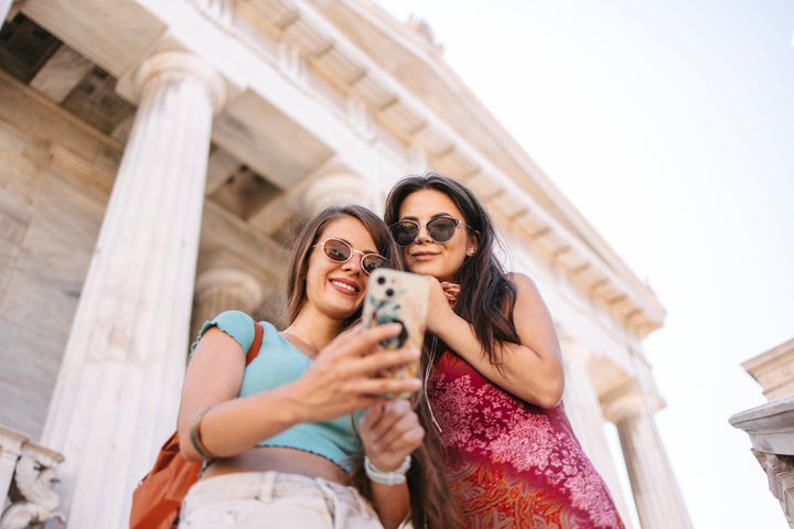 Two female friends in front of a National Library of Greece in Athens looking at the phone