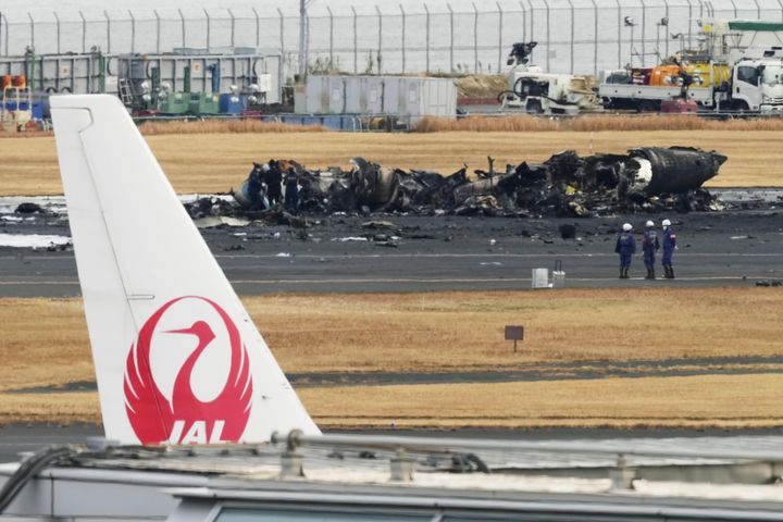 Το καμένο αεροσκάφος της ιαπωνικής ακτοφυλακής φαίνεται στο πίσω μέρος πίσω από το λογότυπο της Japan Airline στο αεροδρόμιο Haneda την Τετάρτη, 3 Ιανουαρίου 2024, στο Τόκιο της Ιαπωνίας. Αξιωματούχοι μεταφορών και αστυνομία ξεκίνησαν την έρευνά τους στο αεροδρόμιο Haneda του Τόκιο την Τετάρτη, αφού ένα μεγάλο επιβατικό αεροσκάφος και αεροσκάφος της ιαπωνικής ακτοφυλακής συγκρούστηκαν στον διάδρομο προσγείωσης και τυλίχθηκαν στις φλόγες, σκοτώνοντας πέντε από τους επιβαίνοντες στο αεροπλάνο της ακτοφυλακής. (Kyodo News via AP)
