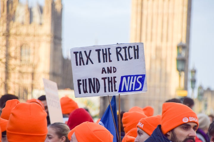 A junior doctor holds a placard which states 'Tax the rich and fund the NHS' at the picket outside St Thomas' Hospital