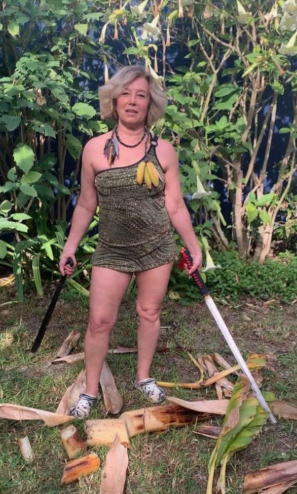 The author wears a short, sparkly costume in her yard while harvesting bananas for a TikTok video.