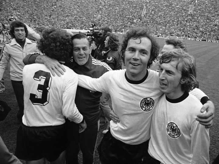 在慕尼黑奥林匹克体育场举行的足球世界杯决赛中，西德队以 2-1 击败荷兰队后，西德国家足球队队长弗朗茨·贝肯鲍尔（右二）在奥林匹克体育场周围散步时拥抱队友前锋尤尔根·格拉博夫斯基，德国，1974 年 7 月 7 日。