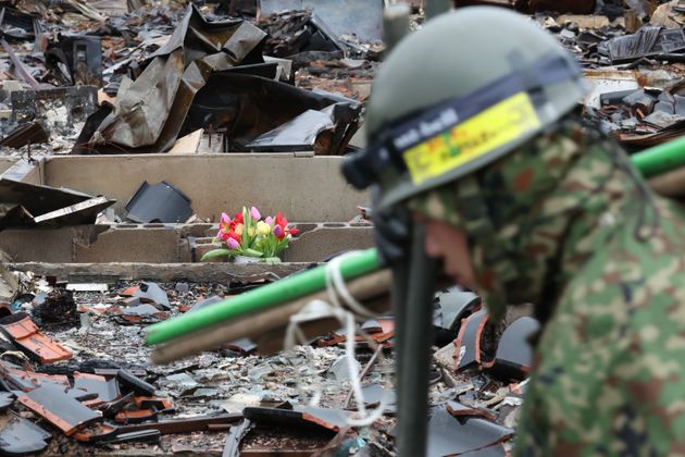 雨が降る中、輪島朝市の焼け跡には花が供えられていた。手前は安否不明者の捜索に向かう自衛隊員＝1月10日午前、石川県輪島市