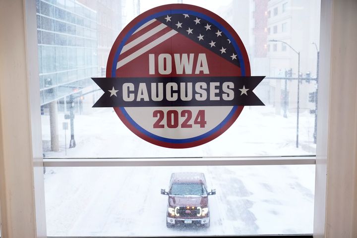 A pickup truck is driven down a snow covered road under an Iowa Caucus sign, Friday, Jan. 12, 2024, in downtown Des Moines, Iowa. (AP Photo/Charlie Neibergall)