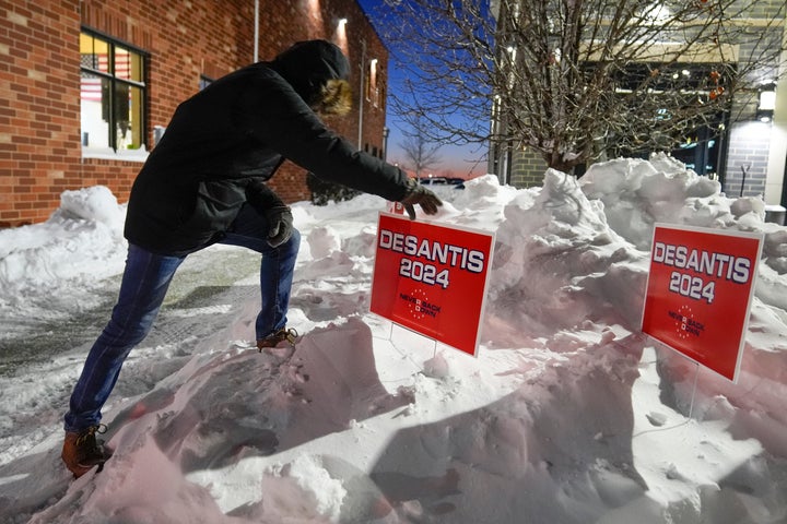 A campaign worker places signs in a snowbank before Republican presidential candidate Florida Gov. Ron DeSantis speaks at a campaign event, on Jan. 14, 2024, in Ankeny, Iowa.