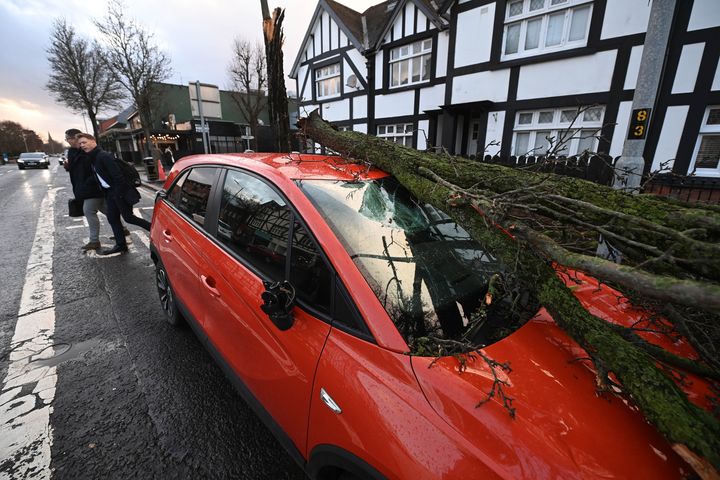 BELFAST: Pedestrians walk past a car damaged by a fallen tree.