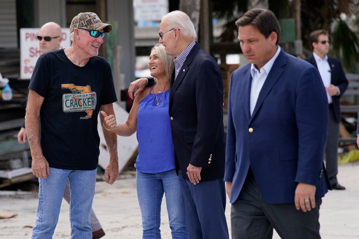 President Joe Biden, center, talks with people affected by Hurricane Ian on Oct. 5, 2022, in Fort Myers Beach, Florida, as Gov. Ron DeSantis (R) walks by at right.