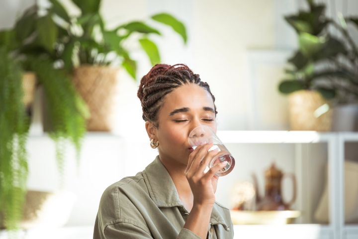 Teenage girl with braided hair sitting on sofa in her room and drinking water.