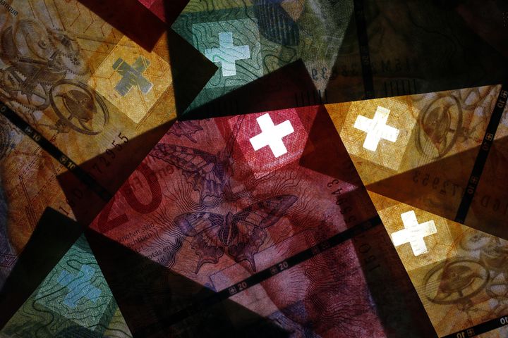 The white cross of the Swiss national flag sits on fifty, twenty and ten Swiss franc banknotes against a black background in Bern, Switzerland. Photographer: Stefan Wermuth/Bloomberg