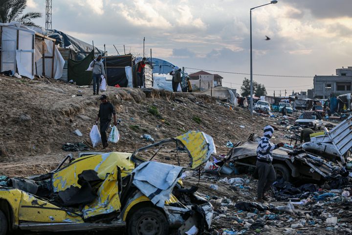 People carry the sacks near the heavily damaged cars after Israeli tanks hit UN Relief and Works Agency for Palestine Refugees (UNRWA) headquarters building in Khan Yunis, Gaza on January 26, 2024. As a result of the Israeli army's tank fire, the building and its surroundings were severely damaged.