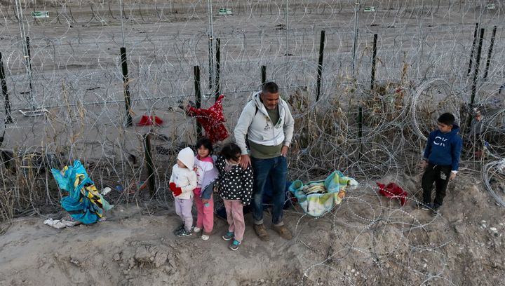 An aerial view shows migrants, including children, walk next to razor wire in Eagle Pass, Texas, after crossing the Rio Grande to seek humanitarian asylum.