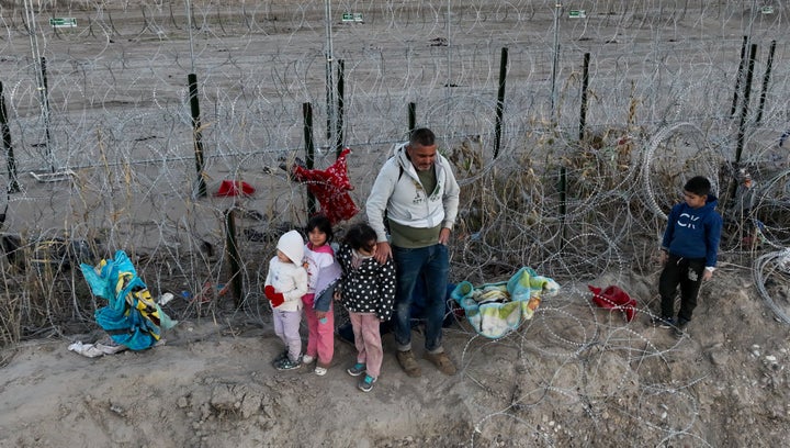 An aerial view shows migrants, including children, walk next to razor wire in Eagle Pass, Texas, after crossing the Rio Grande to seek humanitarian asylum.