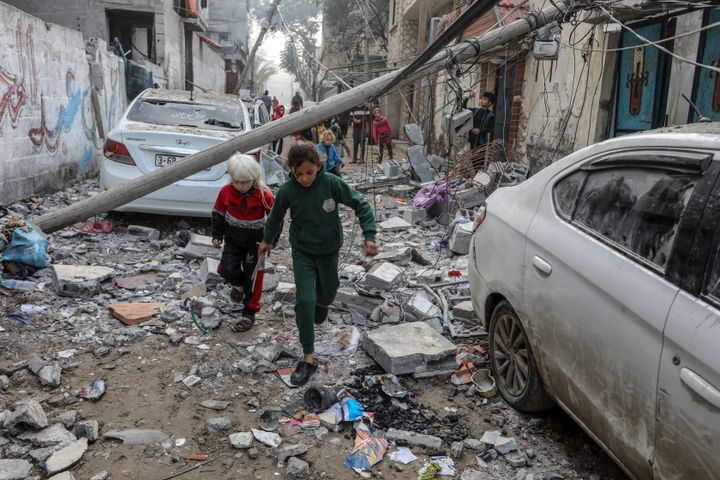 : Παλαιστινιακά παιδιά περπατούν ανάμεσα στα κατεστραμμένα αυτοκίνητα και την πολυκατοικία της οικογένειας al-Mashuhi, μέρος της οποίας κατέρρευσε, μετά τις ισραηλινές επιθέσεις στη Ράφα της Γάζας στις 09 Φεβρουαρίου 2024. Ένα κτίριο που έγινε στόχος της ισραηλινής επίθεσης και άλλες κατασκευές γύρω από αυτό υπέστησαν ζημιές.