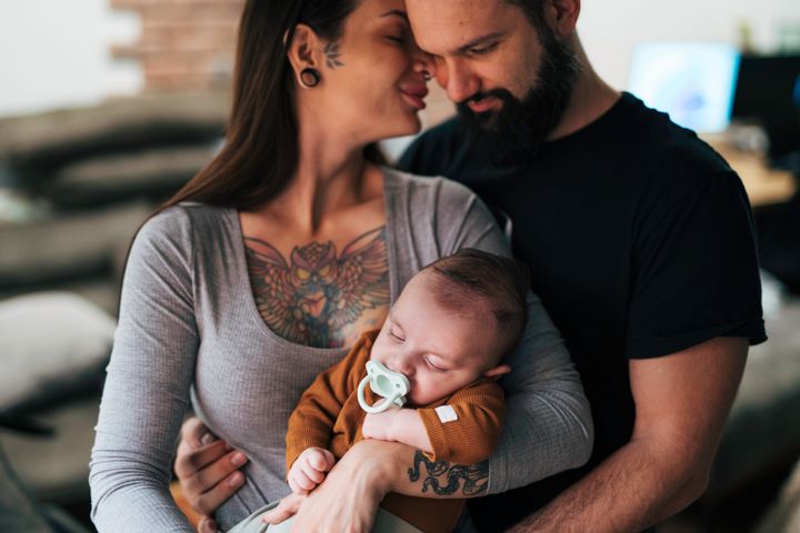 Young happy couple with baby. Woman has tattoos on her chest. Baby is sleeping.