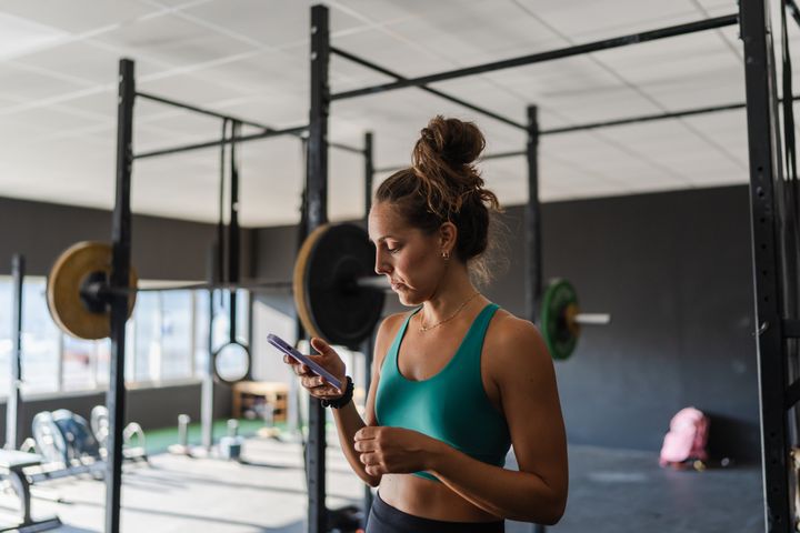 woman looks intently at her cell phone during a break in her fitness workout at the gym