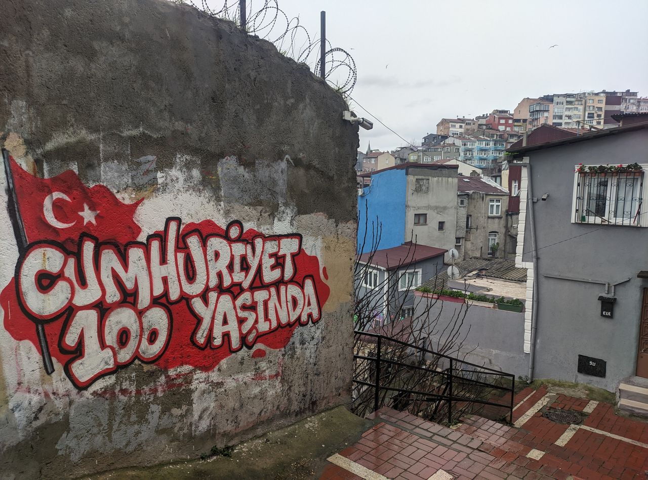 «Cumhuriyet 100 Yaşında» (μτφ. Δημοκρατία 100 ετών) γράφει το σύνθημα στον τοίχο από την επέτειο του 2023 για τον έναν αιώνα από την ίδρυση της σύγχρονης Τουρκίας. Στο βάθος η πολύχρωμη συνοικία Μπάλατ.
