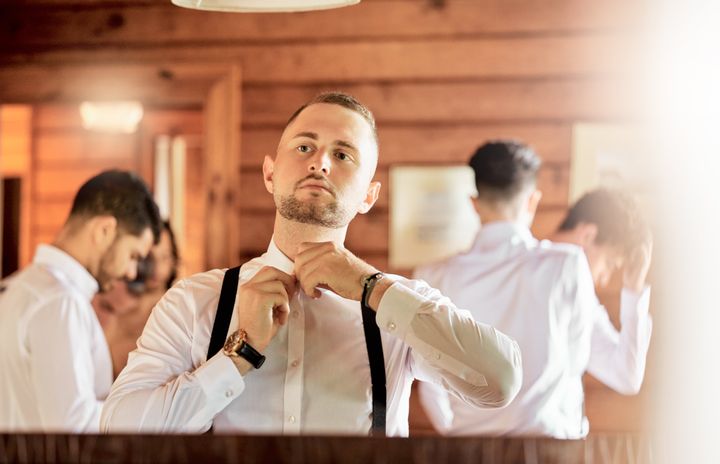 Wedding, clothes and mirror reflection of man prepare and fix shirt button before start of marriage celebration. Group of people, friends or groomsmen ready for partnership, trust or commitment event