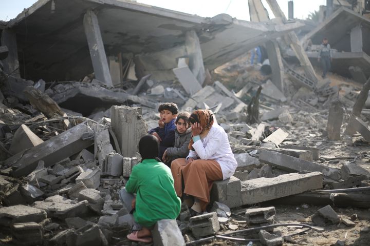 2024年2月12日、イスラエルによるガザ地区ラファへの砲撃で破壊された建物のかたわらに座るパレスチナ人たち