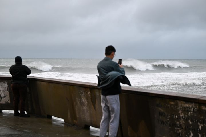 People are seen during heavy rain as massive waves hit the coast and high surf and coastal flood warning issued, in Pacifica, California, on Feb. 18, 2024.