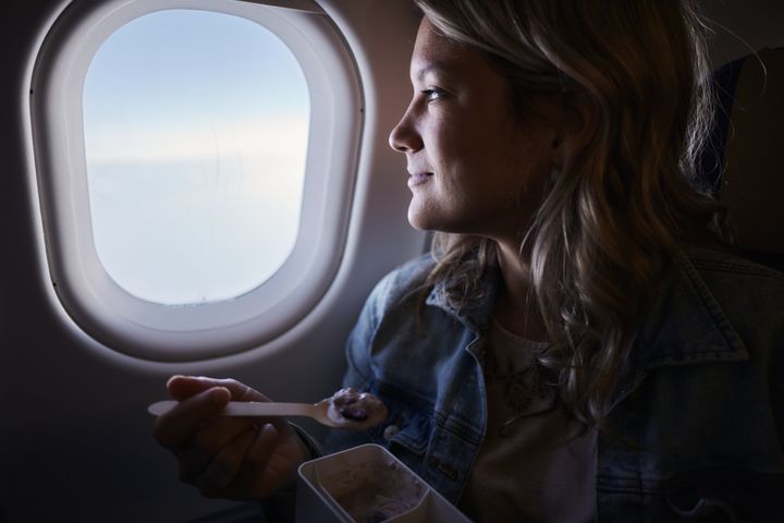 Smiling woman day dreaming while eating a snack during a flight by airplane.