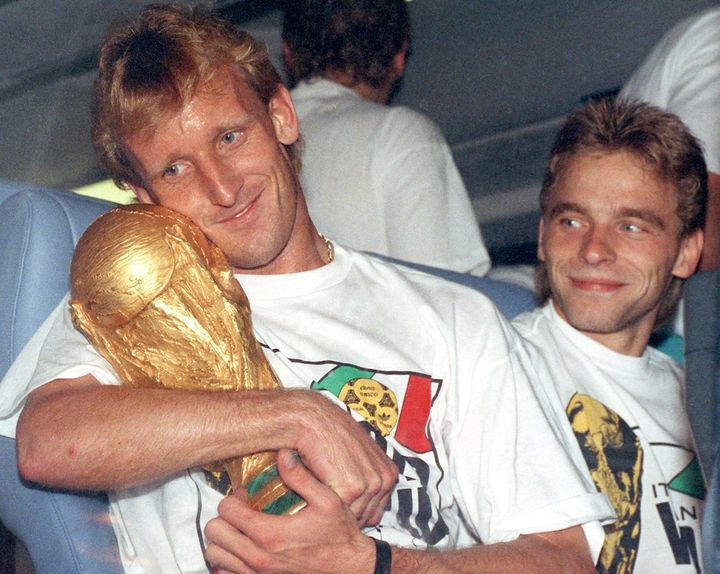 Ο Αντρέας Μπρέμε αγκαλιά με το Παγκόσμιο Κύπελλο του 1990, ενώ δίπλα του στέκεται ο συμπαίκτης του Τόμας Χέσλερ. 