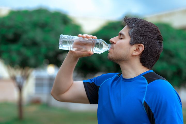 Man in blue sports t-shirt drinking water from plastic bottle and doing sports with copy space