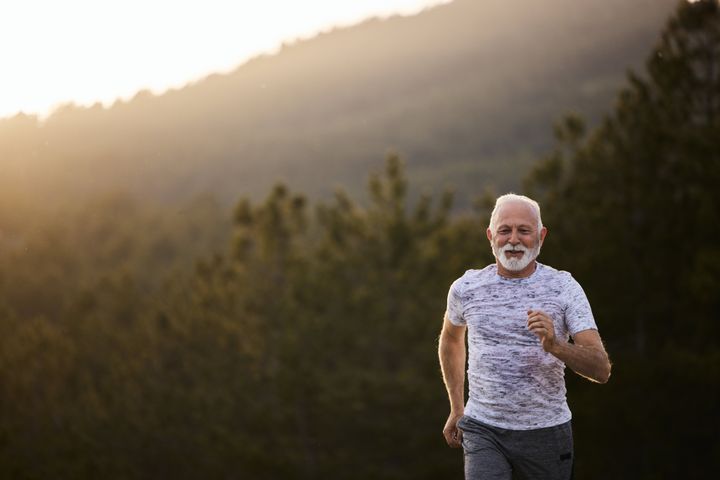 Happy senior man running during sports training in nature at sunset. Copy space.