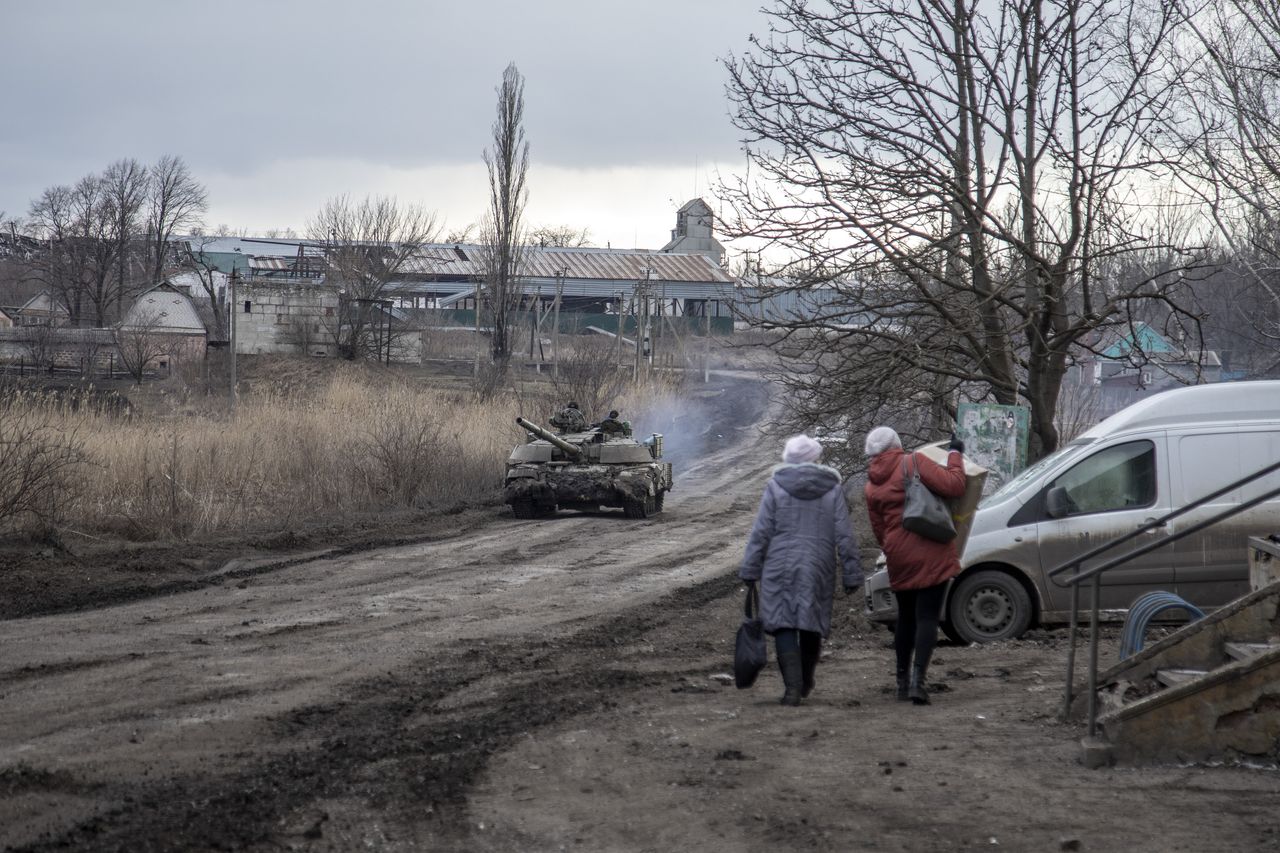 Civilians walk on a road as a tank drives by in a village nearby Avdiivka frontline.