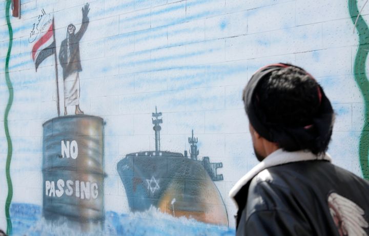 A man walks next to artwork in Sana'a, Yemen, depicting a Yemeni checkpoint stopping an Israeli vessel in the Red Sea, in solidarity with Palestinians and against the U.S.-led aerial attacks, on February 25, 2024. The U.S. and U.K. launched fresh aerial attacks jets targeting 18 sites run by Houthi rebels in the capital and other various provinces.