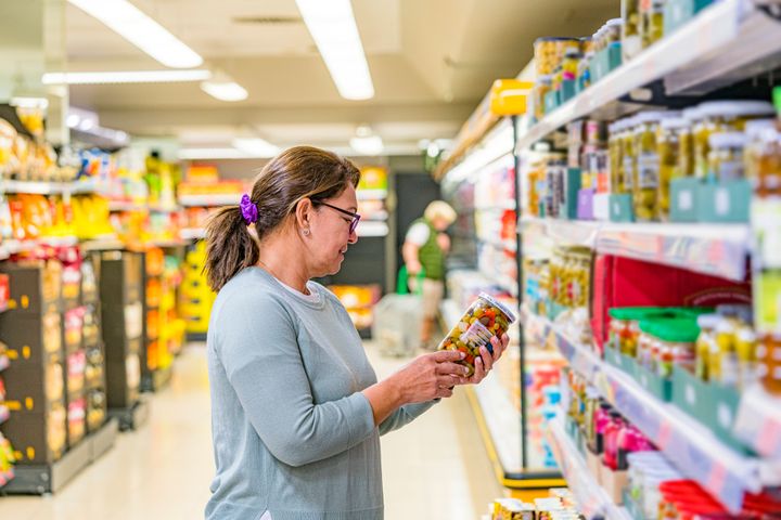 Woman reading label of jar in supermarket