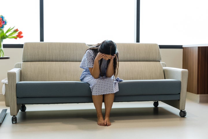 The mid adult woman weeps and mourns alone in her hospital room after losing her baby.