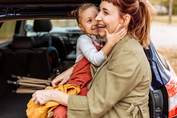 A photo of a mother and her daughter packing backpacks in car, while bonding and sharing love. They are getting ready for hiking adventure.