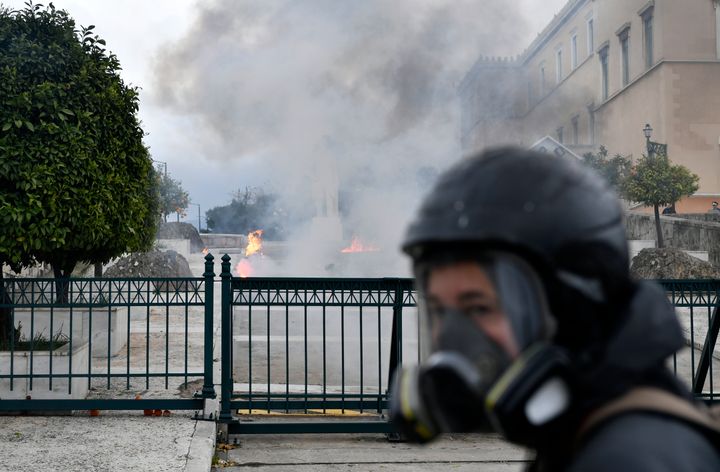 Ένας φωτογράφος με μάσκα και κράνος περνά μπροστά από τις φλόγες αφού διαδηλωτές πέταξαν βόμβες μολότοφ στο ελληνικό κοινοβούλιο κατά τη διάρκεια της συγκέντρωσης στην Αθήνα, Ελλάδα, Τετάρτη, 28 Φεβρουαρίου 2024. Οι εκτεταμένες απεργίες στην Ελλάδα διέκοψαν τις συγκοινωνίες την Τετάρτη. Οι διαμαρτυρίες οργανώθηκαν με αφορμή την επέτειο του θανατηφόρου σιδηροδρομικού δυστυχήματος στα Τέμπη, πριν από ένα χρόνο. (AP Photo/Michael Varaklas)