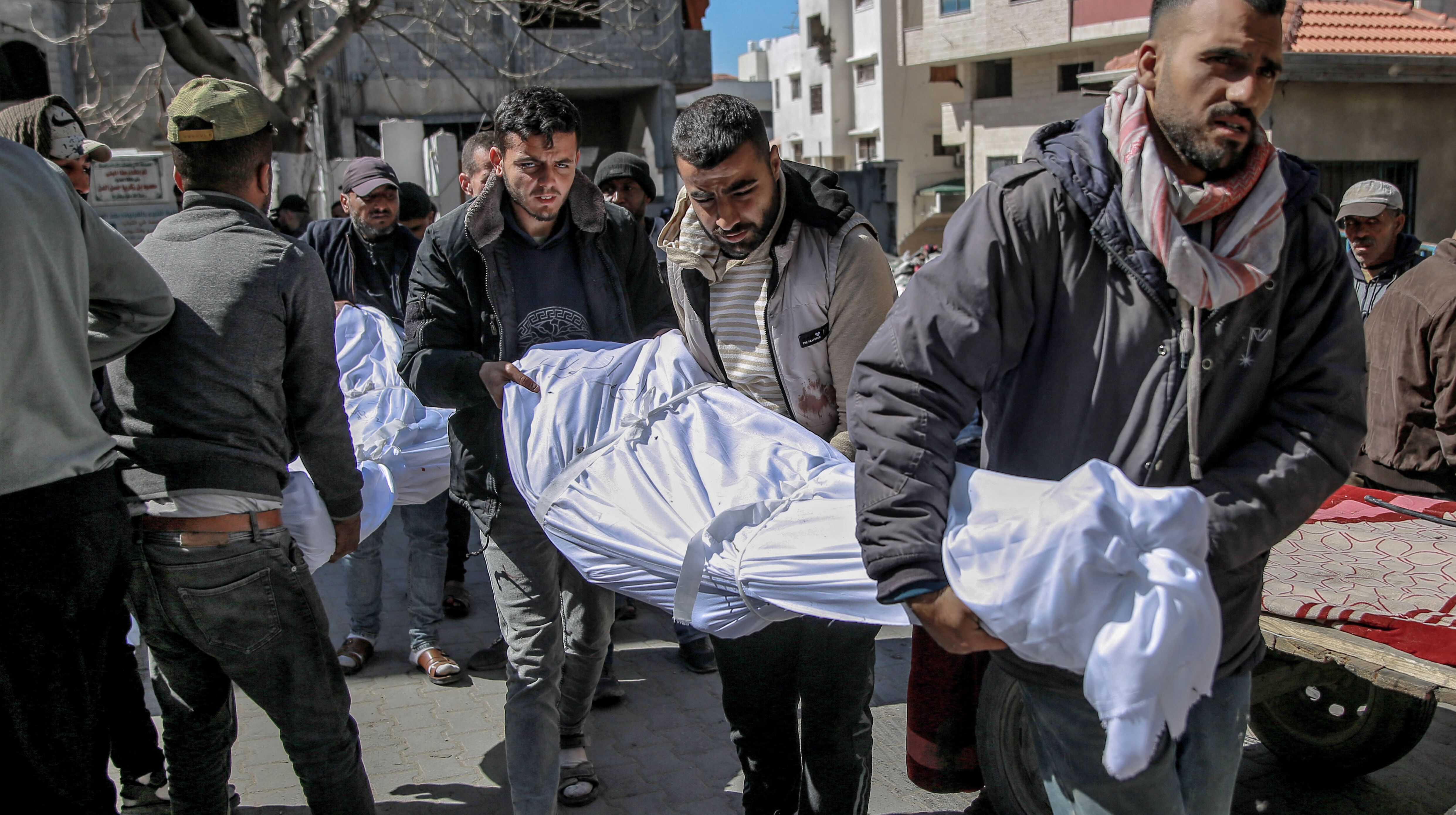 Men carry the bodies of people killed in an early morning incident when residents rushed toward aid trucks in Gaza City on February 29, 2024. 