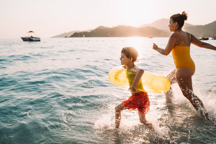 Young mother with little son runs into the sea on sunset light.