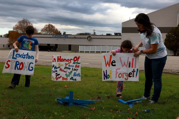 Bre Allard, along with her children Zeke Allard, 8, and Lucy Allard, 5, place crosses and signs in front of the bowling alley where Card killed seven people.