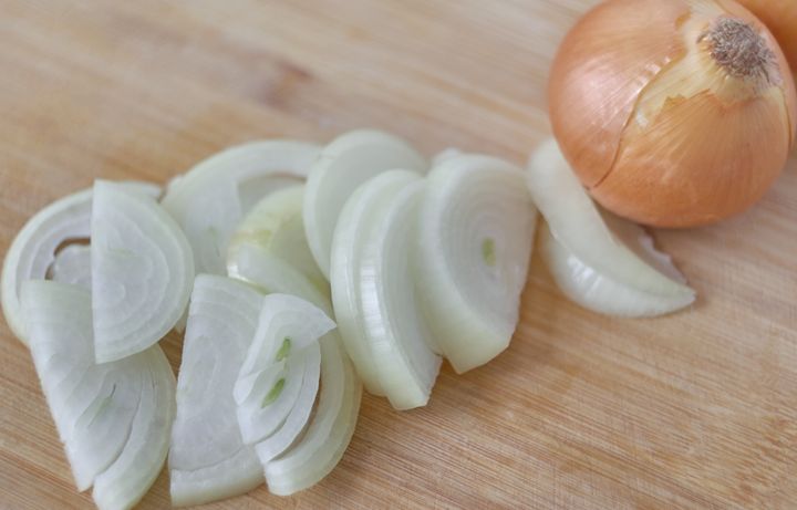 Close-up of onions being thinly sliced on a cutting board.