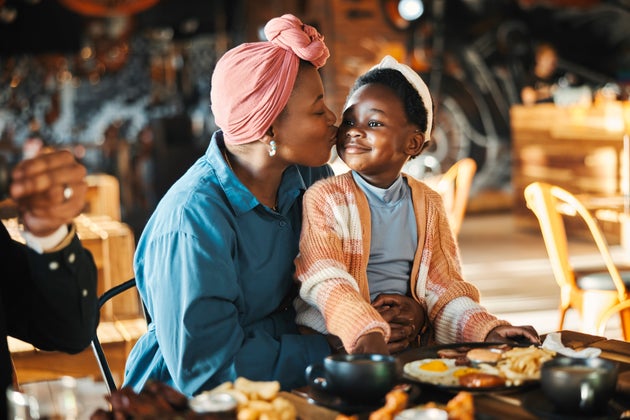 Black family, restaurant and eating with mom kiss and child together with bonding, food and care. Love, diner and table with burgers and happy girl with lunch and hungry people in a cafe with drink