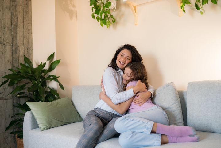 A happy mother and her daughter hug each other while sitting on sofa at home